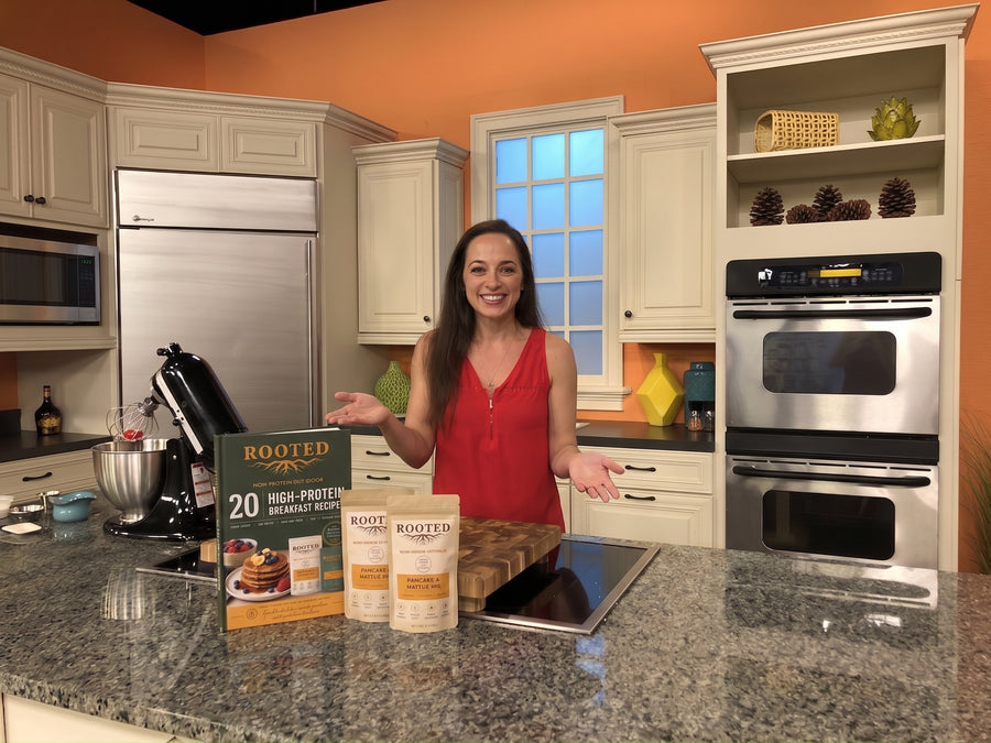 Woman presenting the Rooted 20 High-Protein Breakfast Recipes ebook and Rooted products in a kitchen