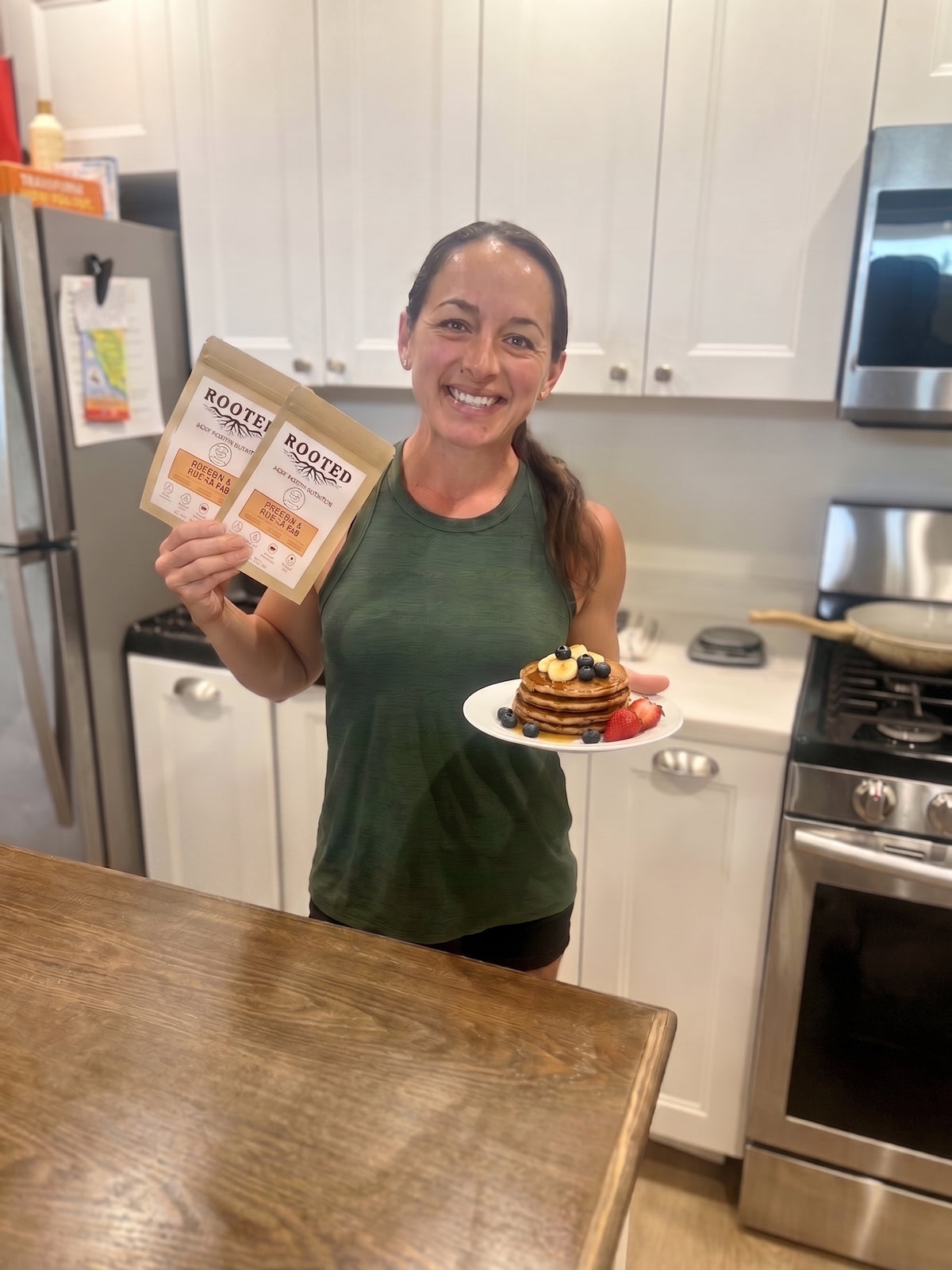Woman holding Rooted pancake mix pouches and a plate of protein pancakes with berries